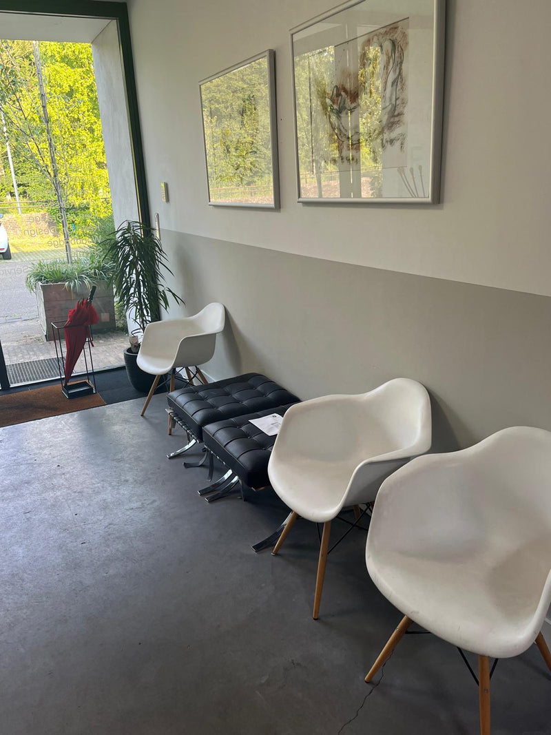 Ontvangstruimte met witte stoelen en zwarte bank bij raam